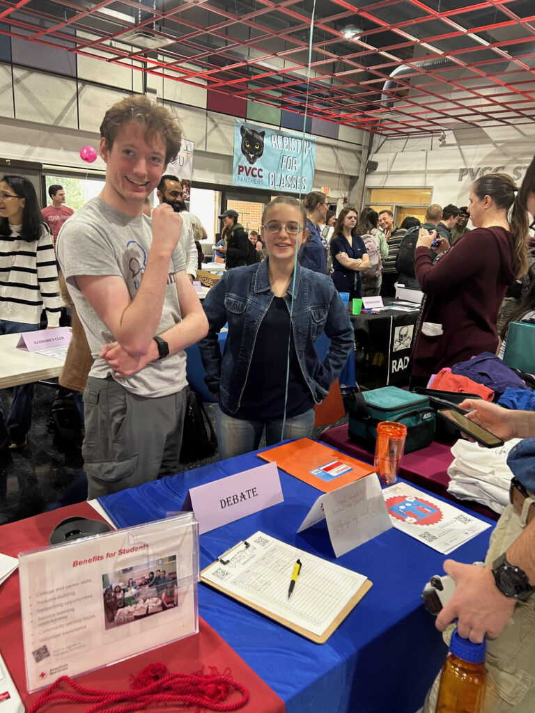 Two students are standing behind the Debate Club display table.