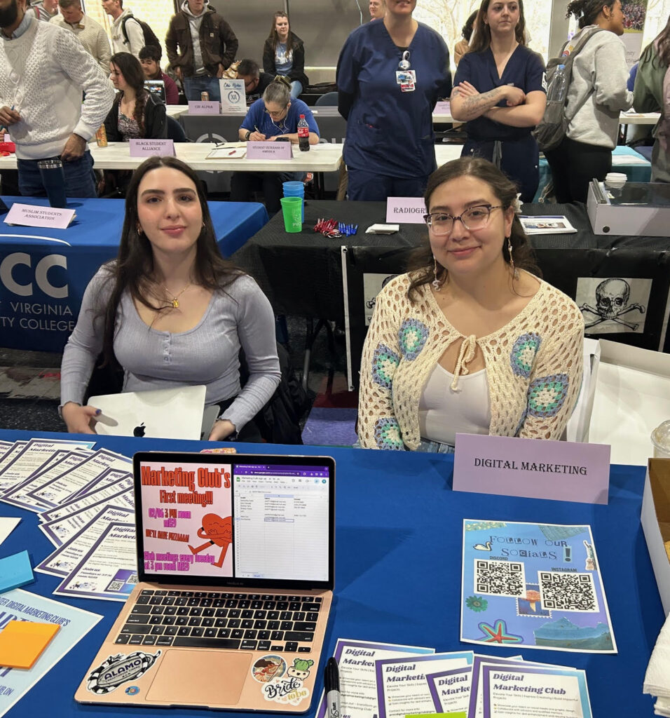 Two students sit behind the Digital Marketing Club display table.