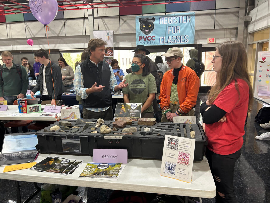 A man talks with his fellow Geology Club members behind the accompanying display table.