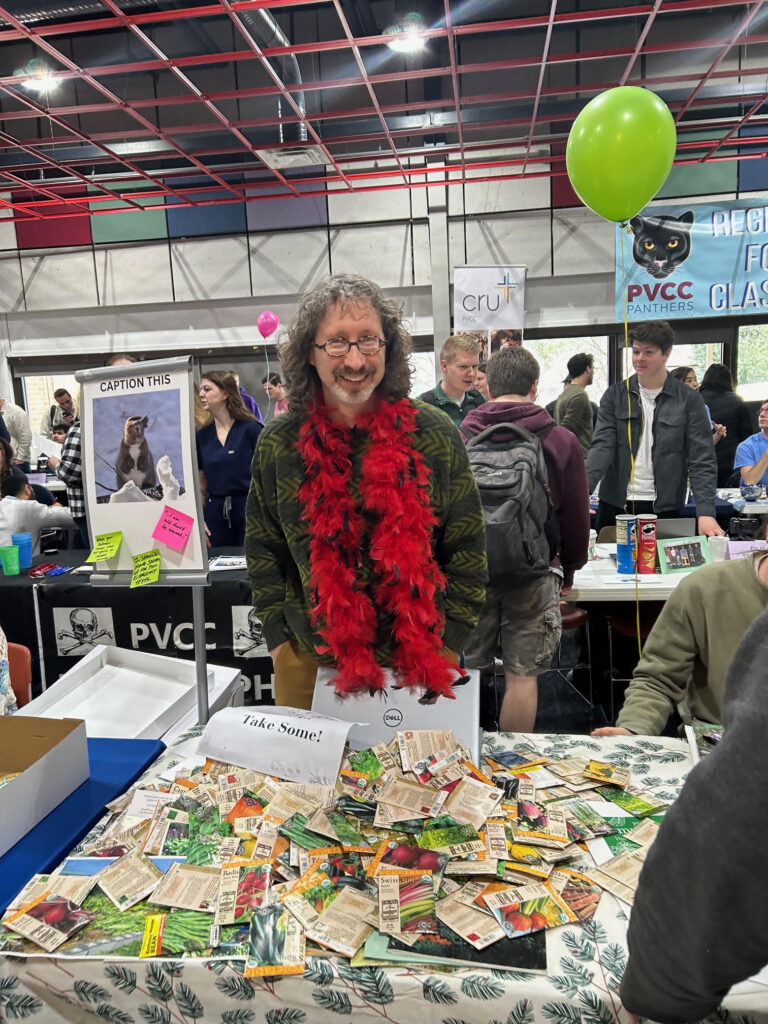 A man with long hair stands smiling with his display for the PVCC Horiculture club.