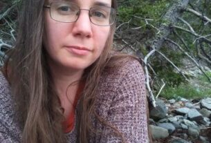 A woman in a sweater sits in nature looks at the camera