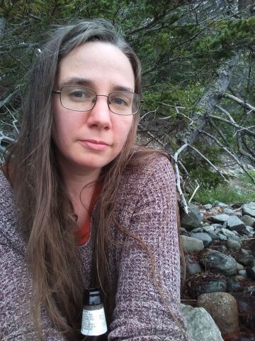 A woman in a sweater sits in nature looks at the camera