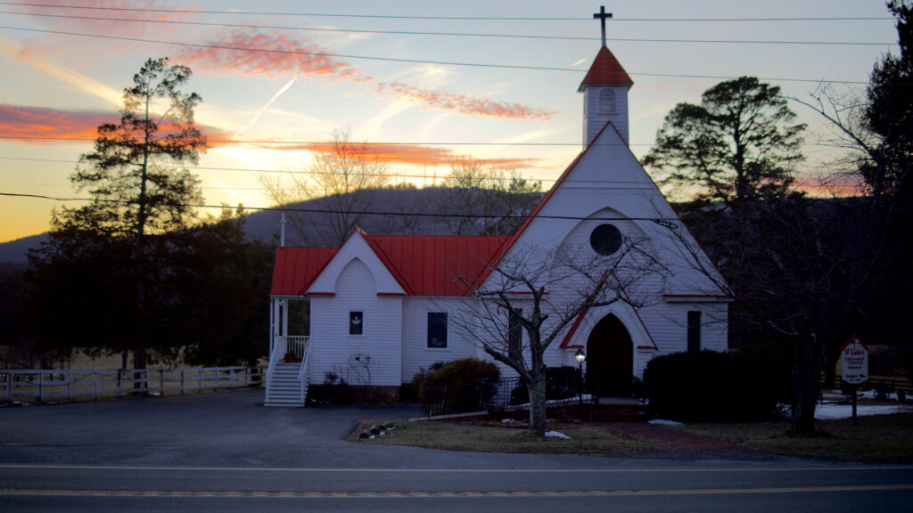 A church with a red roof sits on the foot of the mountainside.