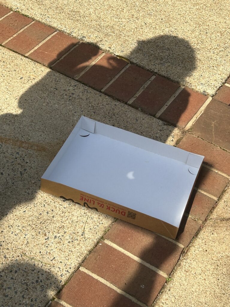 A Duck Donuts box on the ground being used a an eclipse viewing tool