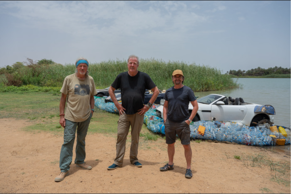 Three middle-aged men stand in front of three sports cars modified to be rafts out of recycled materials.