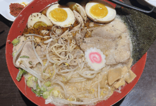 A red bowl of ramen with eggs and meat