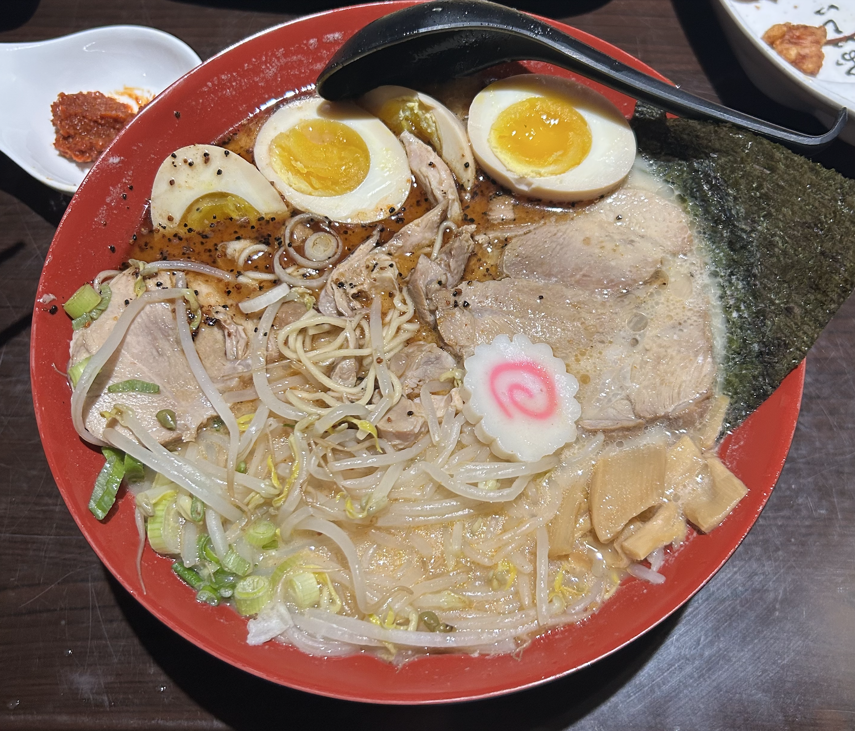 A red bowl of ramen with eggs and meat