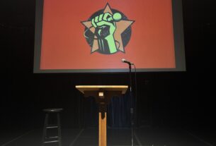 Podium and microphone for One Mic Stand in front of a screen that shows a hand holding a mic against a red background