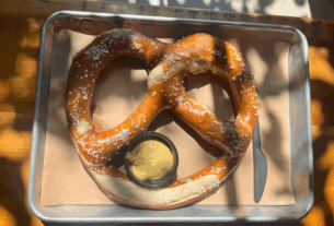 A large pretzel on a silver tray with a cup of mustard
