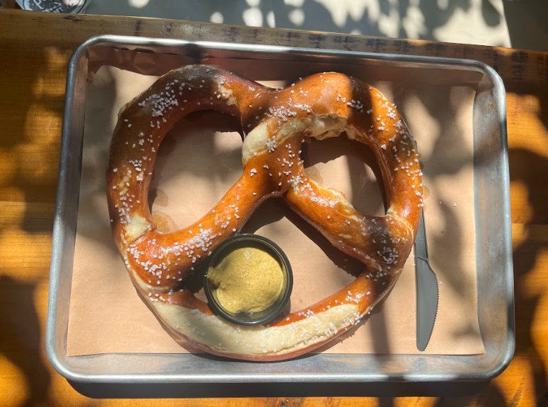 A large pretzel on a silver tray with a cup of mustard