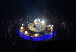 Tyler Childers playing guitar in a spotlight surrounded by fans in the dark