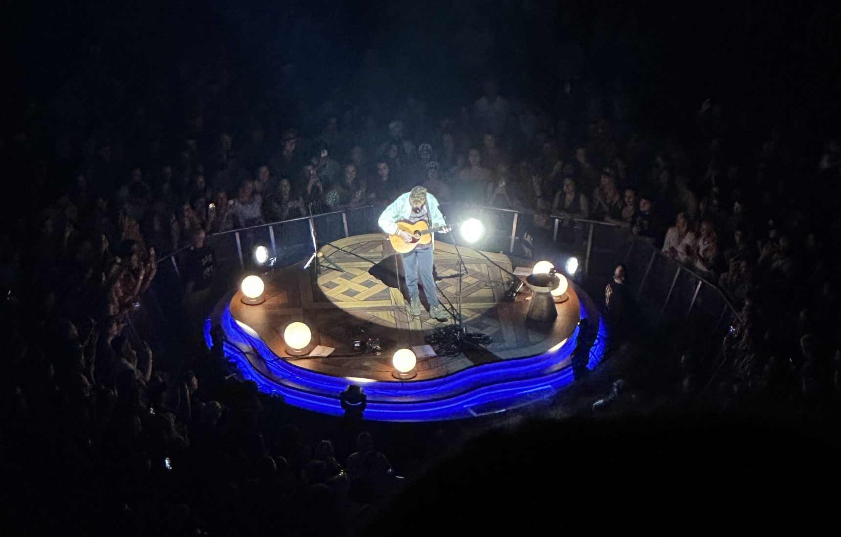 Tyler Childers playing guitar in a spotlight surrounded by fans in the dark