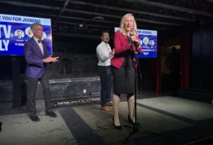 Abigail Spanberger, stands on a stage with Bill Nye and Pete Buttigieg standing behind her.