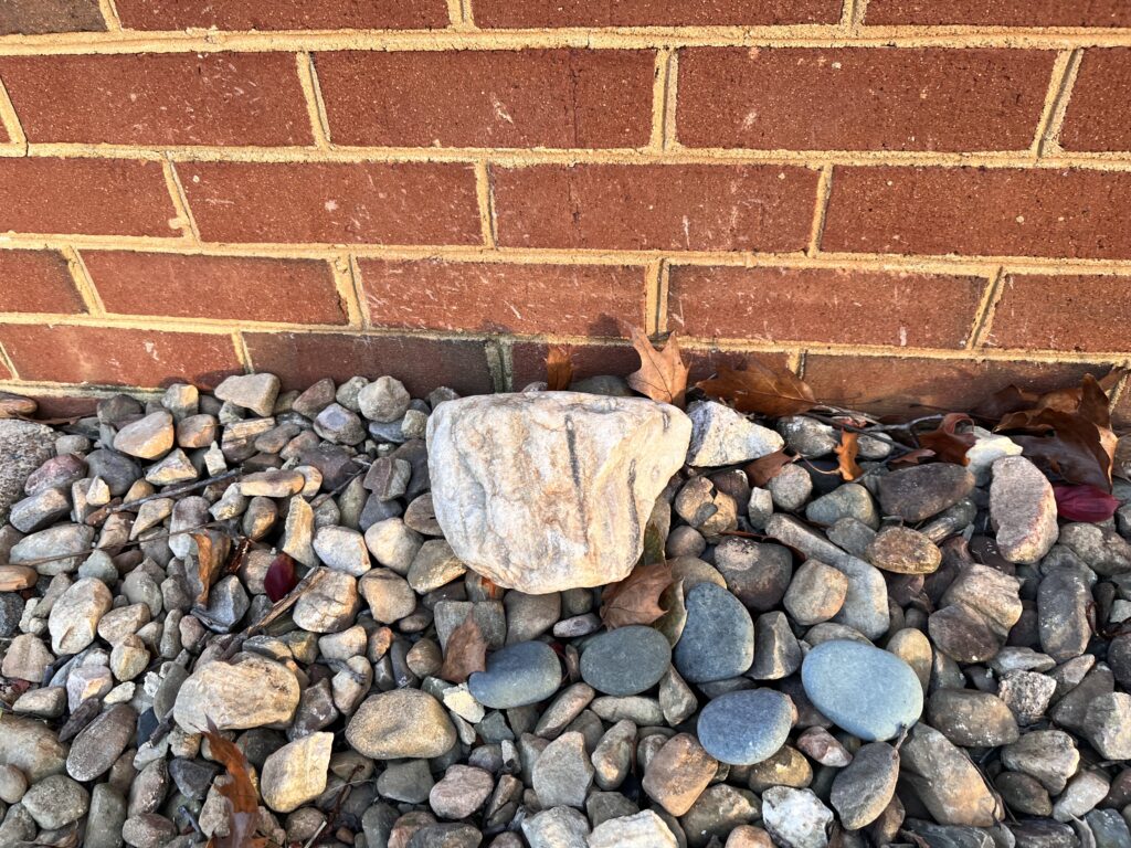 A larger piece of sandstone sits on top of small rocks next to a brick wall