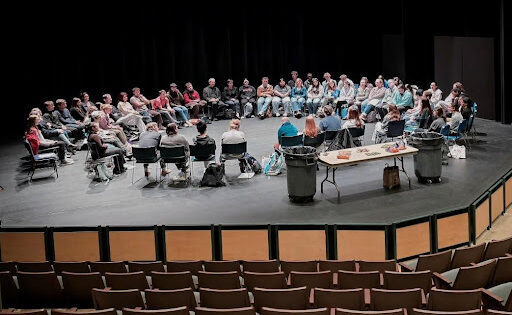 a large circle of people sitting on chairs facing each other on the Dickinson stage