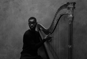 a black and white photo of Dave wearing a black shirt and posing with his harp