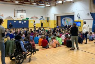 Broadus Wood Elementary School’s Gymnasium filled with students and faculty sitting on the floor watching a presentation