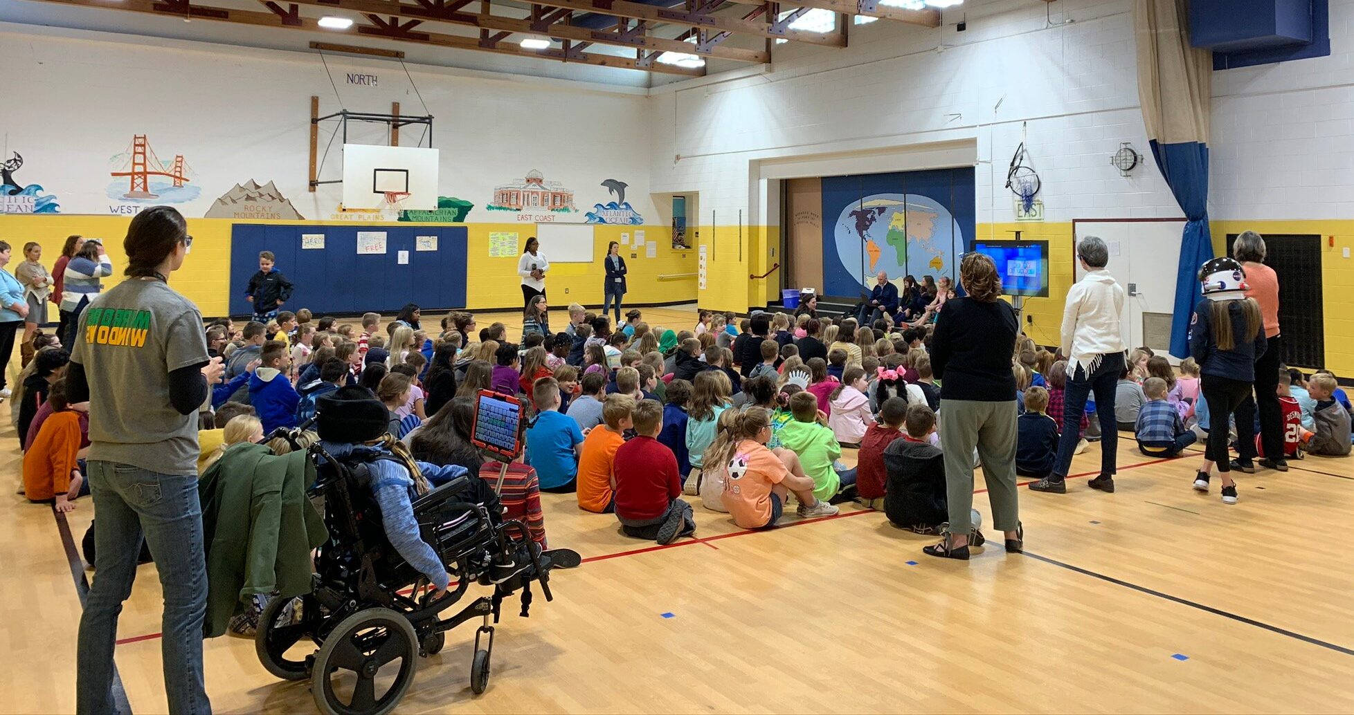 Broadus Wood Elementary School’s Gymnasium filled with students and faculty sitting on the floor watching a presentation