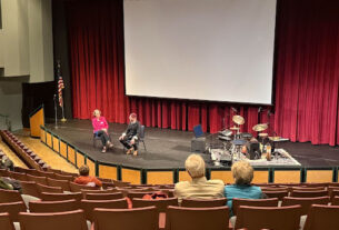 Tom Teasley sits on stage with Fenella Belle with instruments off to the side.