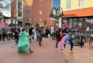 Lady Liberty and other participants dancing on their way back to Ting Pavilion while holding American flags.