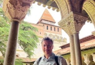 Jorge Grajales-Diaz poses smiling under an arch int the cloister at Saint-Pierre de Moissac, France