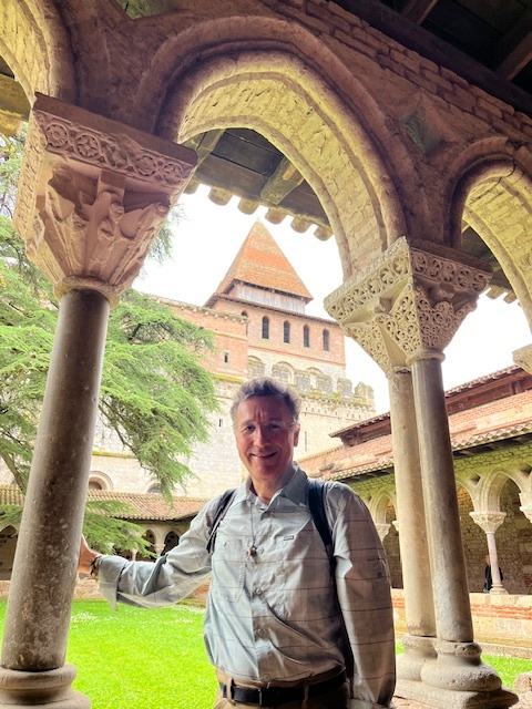 Jorge Grajales-Diaz poses smiling under an arch int the cloister at Saint-Pierre de Moissac, France