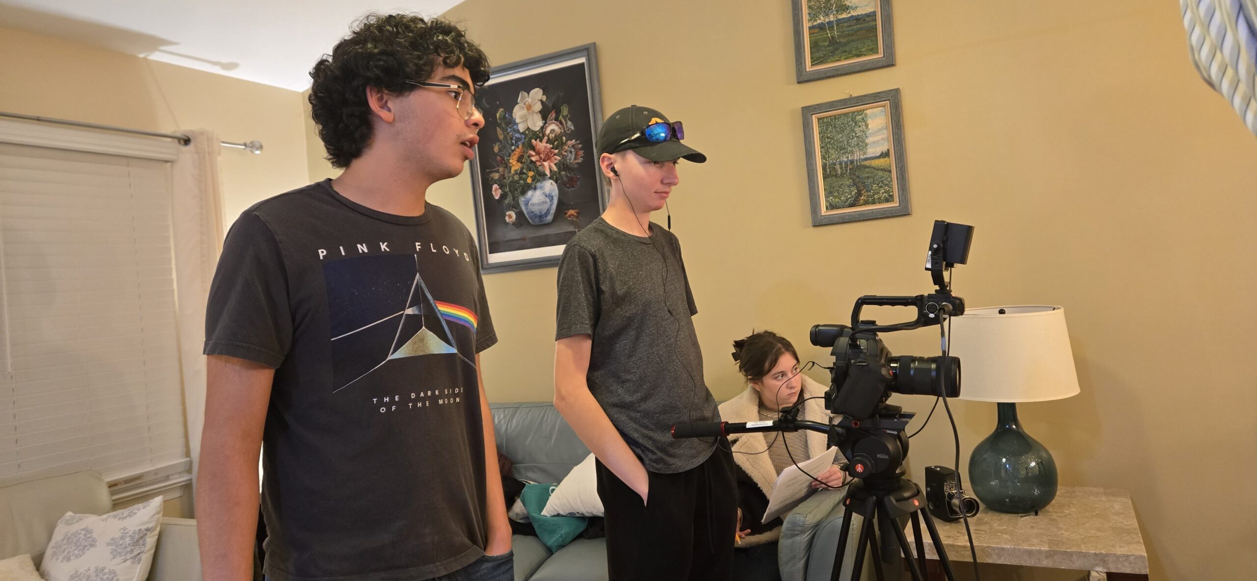 Three students behind a video camera with one holding a script.