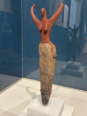 A clay sculpture of a female figure with her arms raised in the sky like a dance.