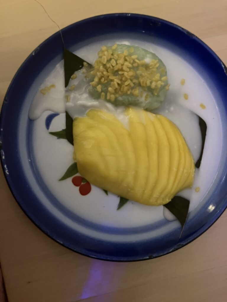 A plate with sliced mango, green rice, and white sauce.