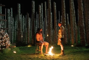 Dr. Kelson speaks with a sedated Samson around a campfire in the bone temple.