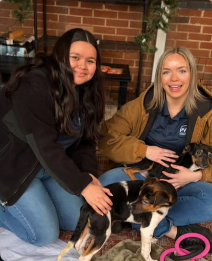 Two PVCC students smile while petting two puppies