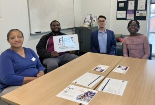 Four people sitting around a table. One person is holding a sign that says "First Generation."