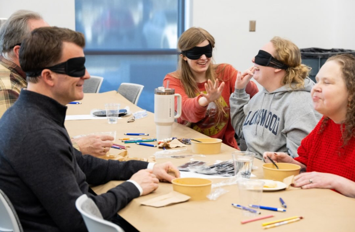 Dr. Sandra Bullins sitting with four smiling blindfolded members of the PVCC community.