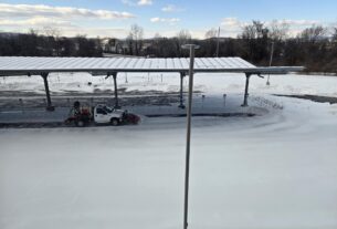 A PVCC truck equipped with a snowplow clearing a parking lot covered in snow.