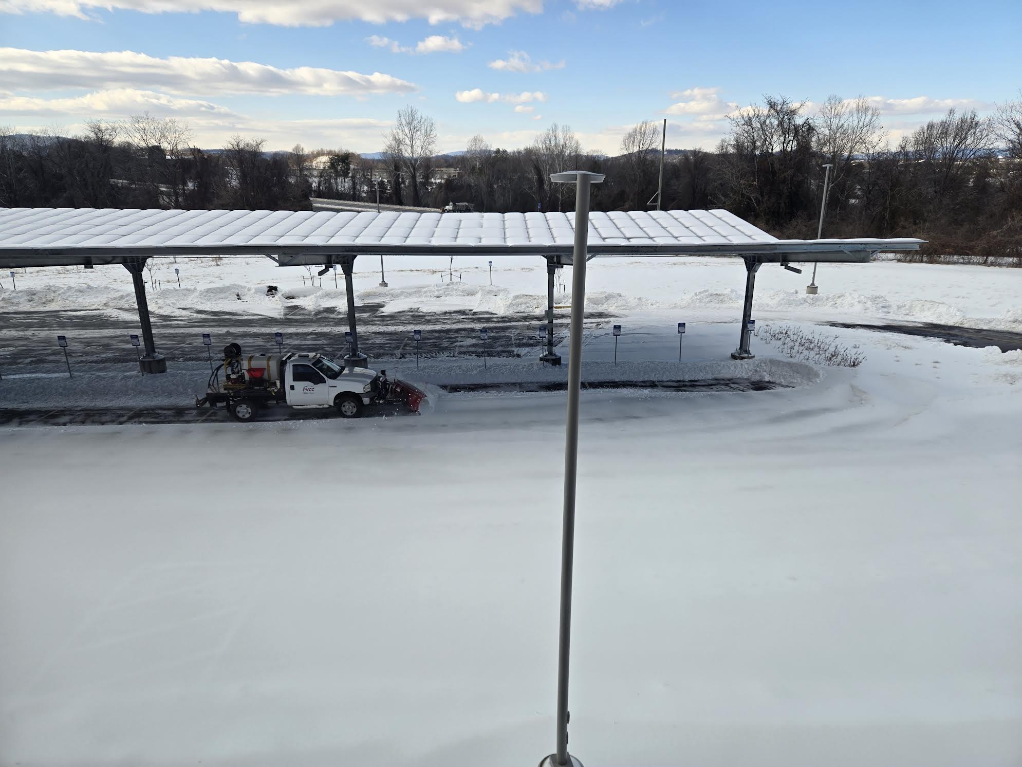 A PVCC truck equipped with a snowplow clearing a parking lot covered in snow.