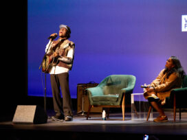 Miles Caton singing while holding a guitar on stage with chairs behind him