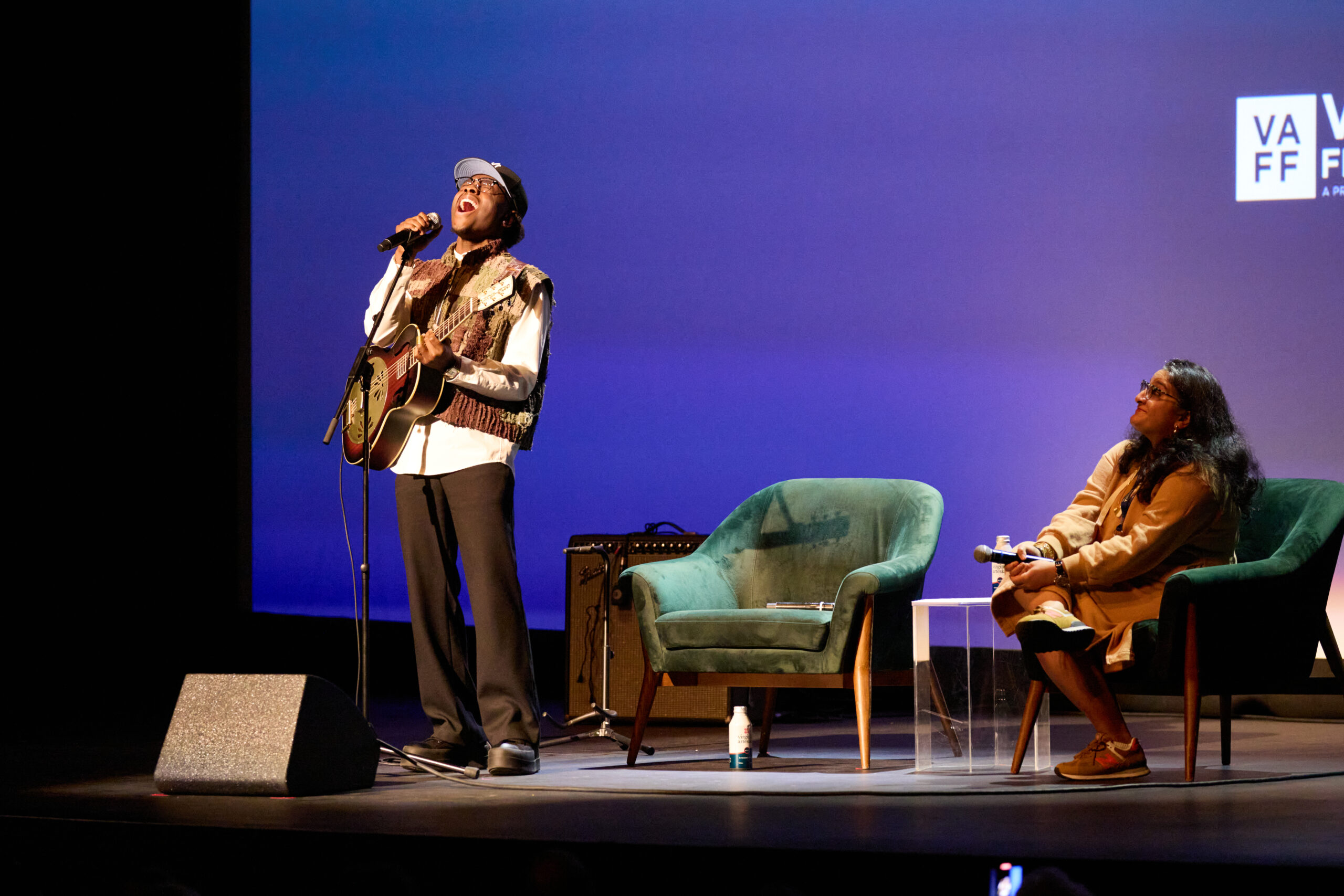 Miles Caton singing while holding a guitar on stage with chairs behind him