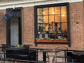 The exterior of a brick building with a patio with several tables and chairs in front.