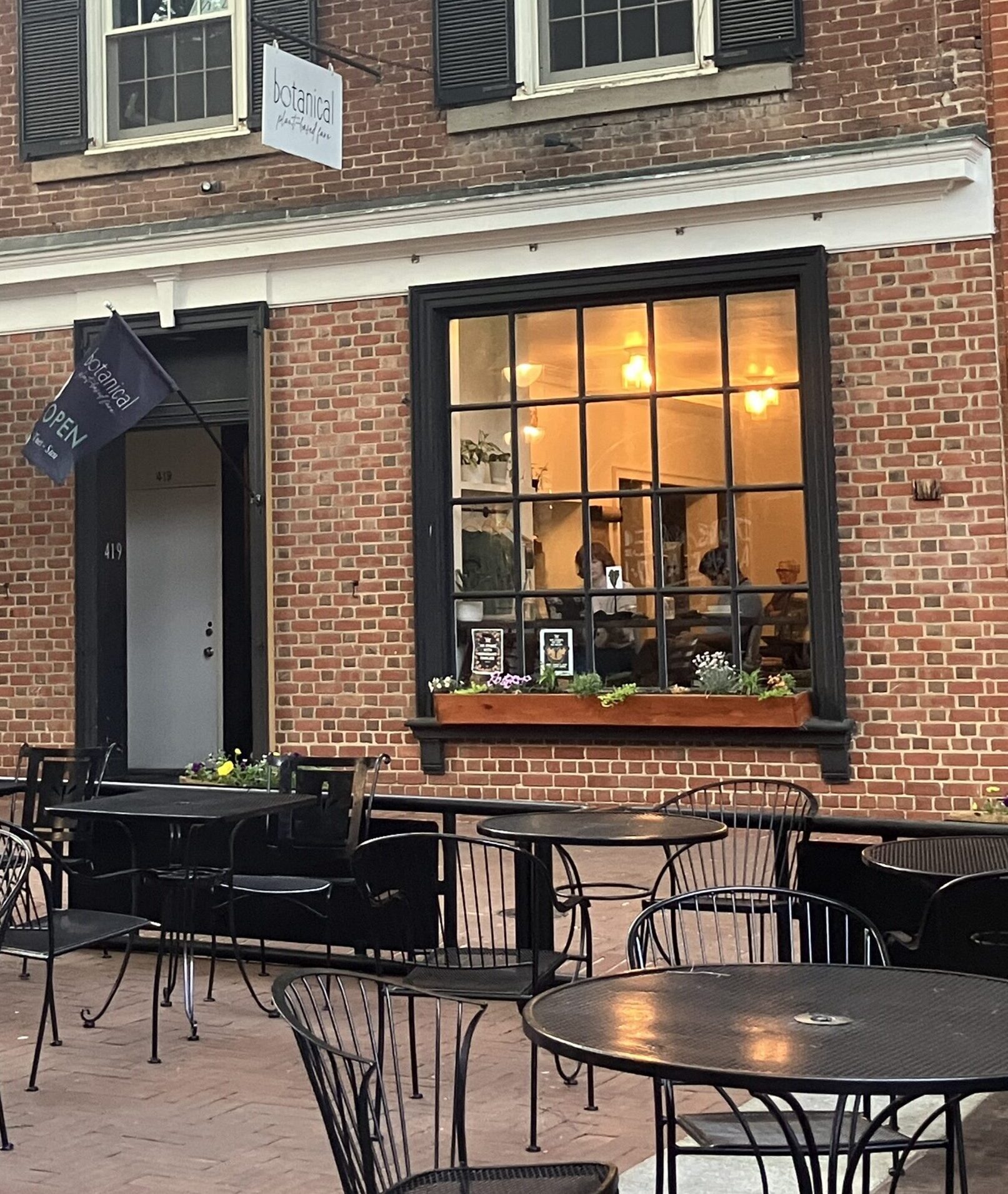 The exterior of a brick building with a patio with several tables and chairs in front.
