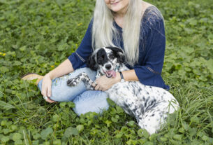 Jamie Reaser sitting on the grass with her black and white spotted dog, Willow.