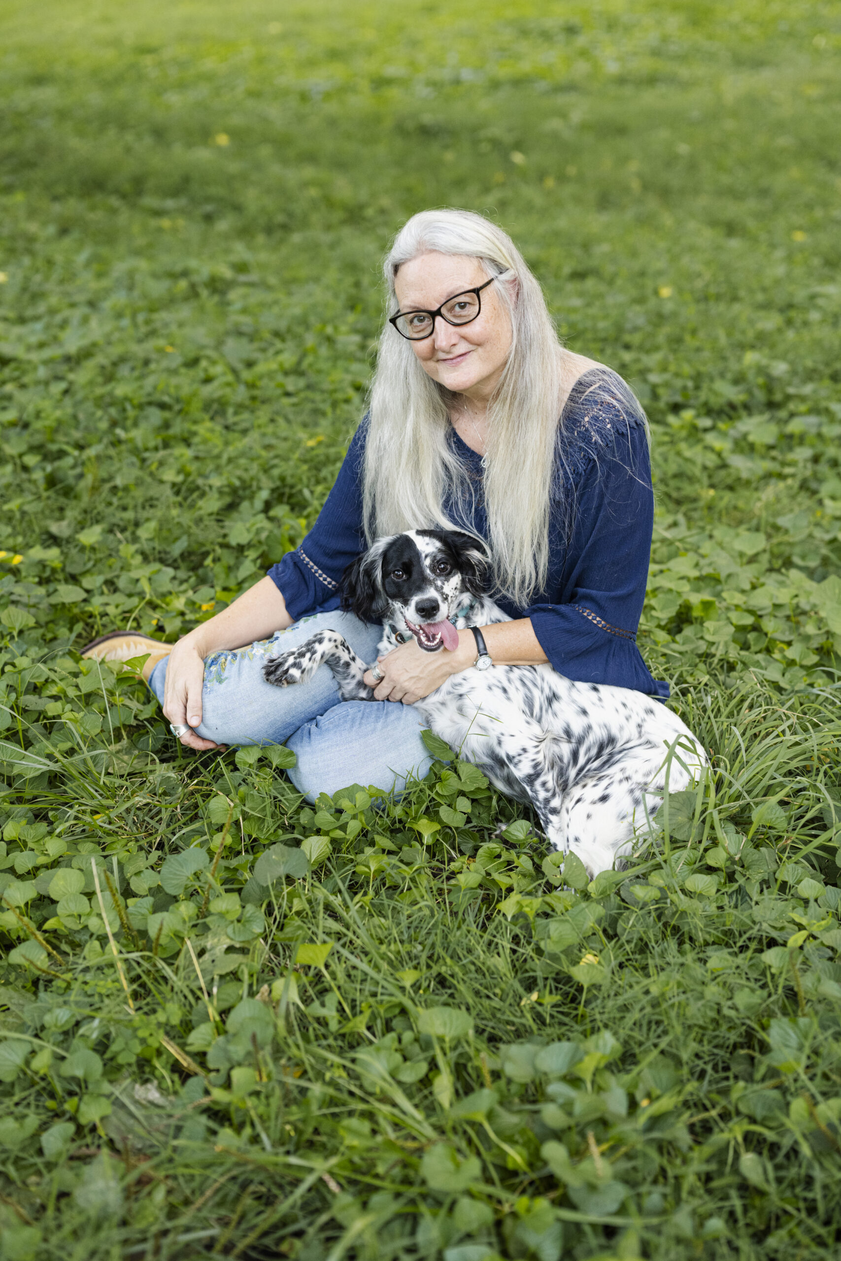 Jamie Reaser sitting on the grass with her black and white spotted dog, Willow.