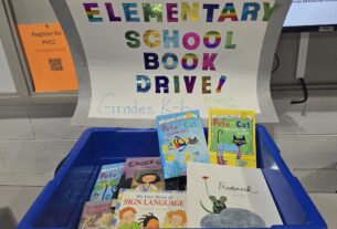 A large, blue bin with children's books in it. A big sheet of paper is connected to the top with "Elementary School Book Drive!" written on it in rainbow lettering.