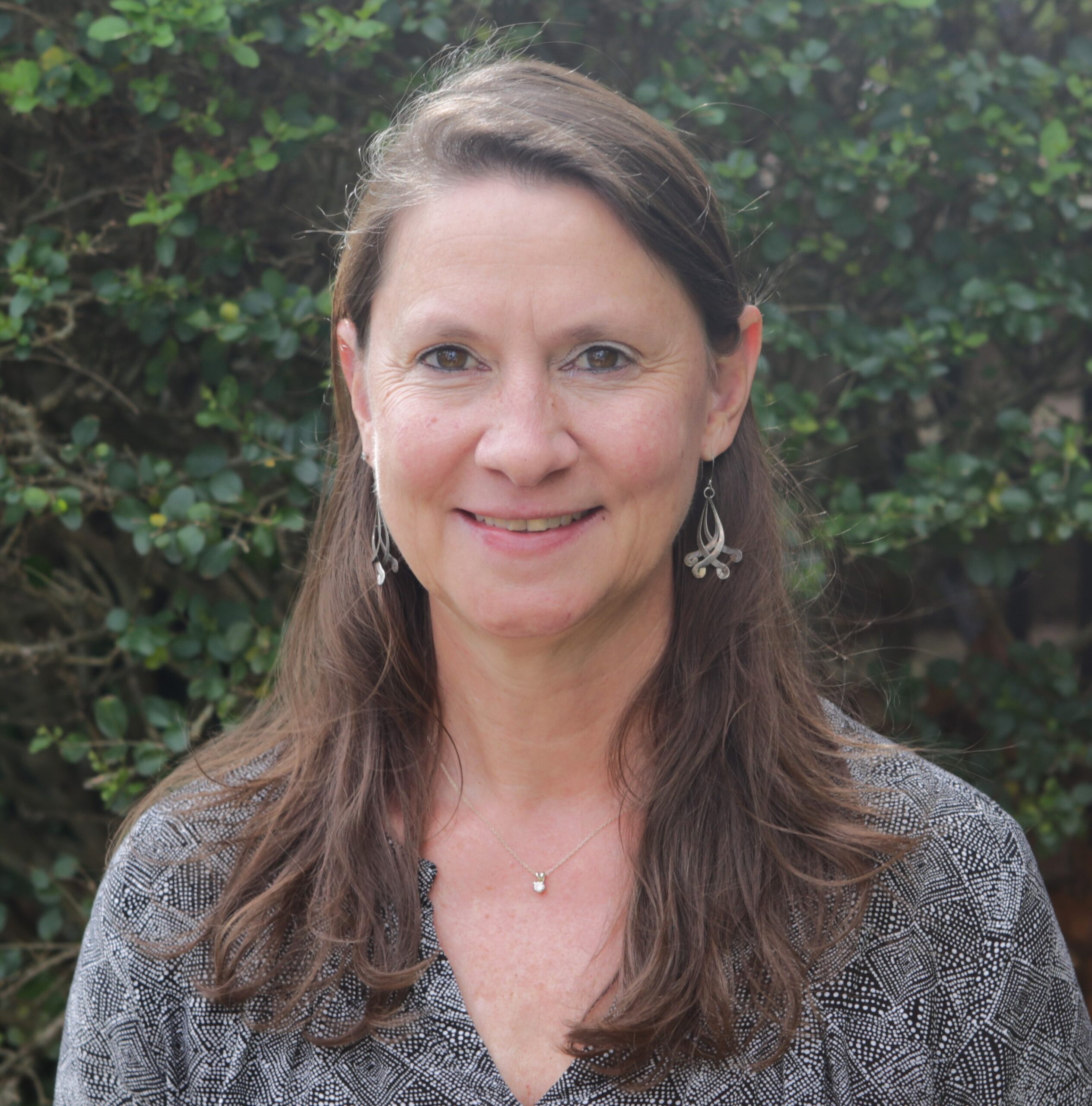 Headshot of Kristel Riddervold taken in front of a leafy background.