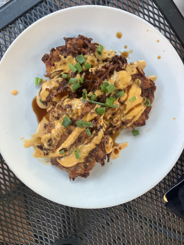 Three flat pancakes with yellow sauce and green scallions on top, served on a white plate. 