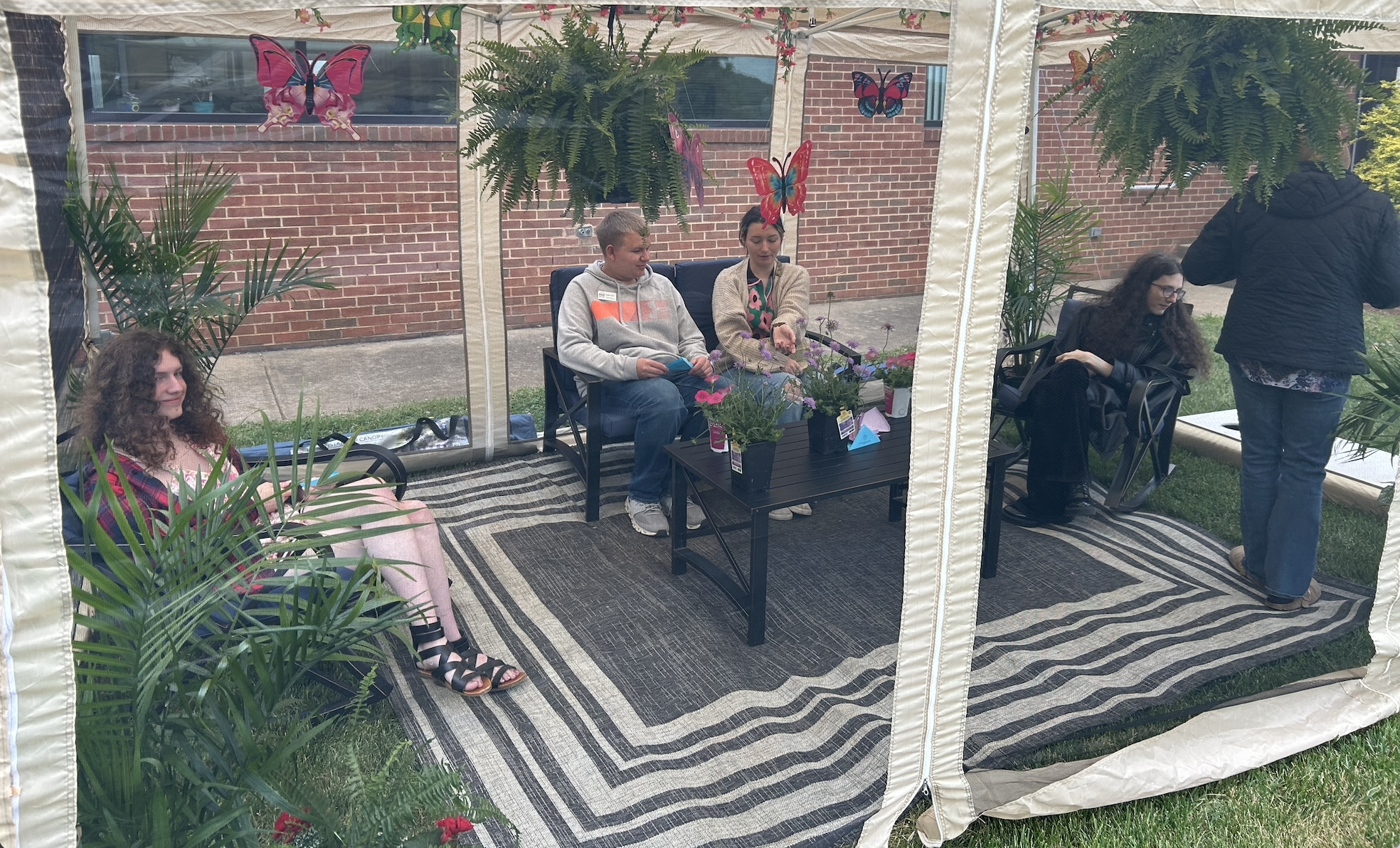Left to right: Sloan Atwell, Braeden Smith, Mycala Hilson, and Monica McGovern sitting in the butterfly tent surrounded by flowers and hanging plants.