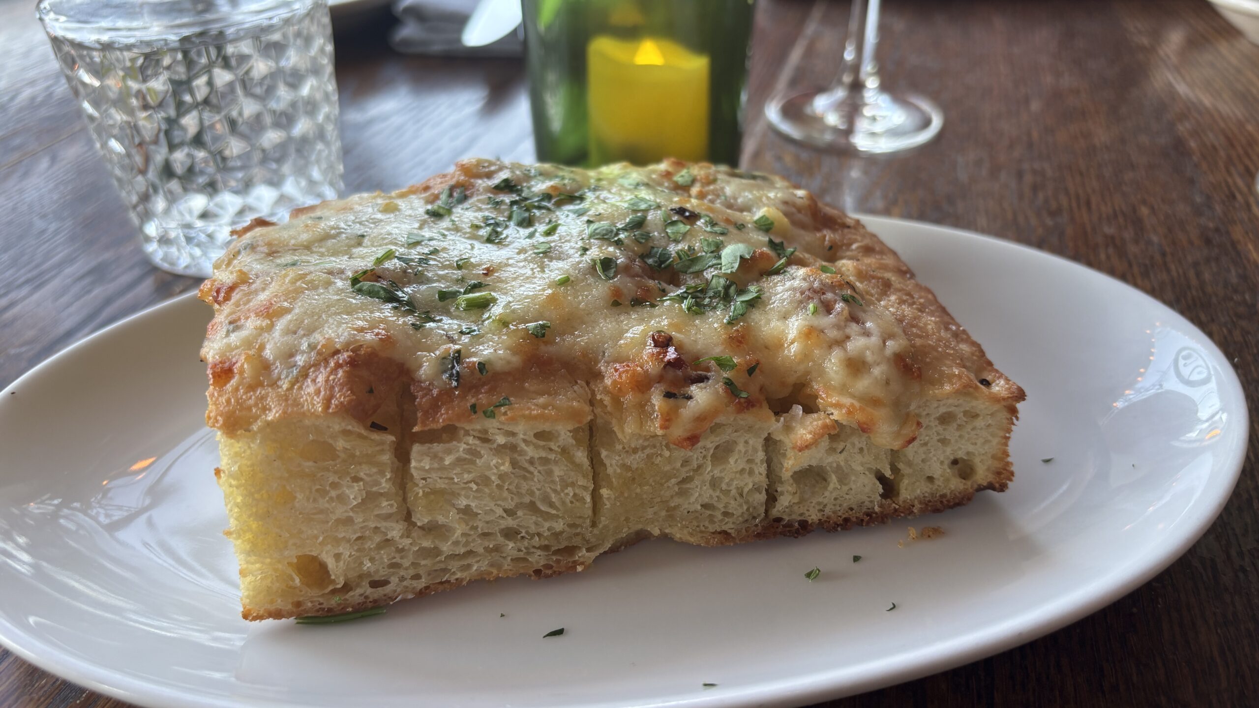 A plate holding fresh-baked focaccia bread split into five sections with garlic butter and topped with herbs and asiago cheese.