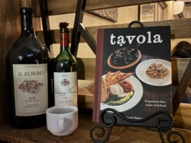 Two bottles of wine, an espresso mug, and a Tavola cookbook displayed behind the host stand at Tavola.