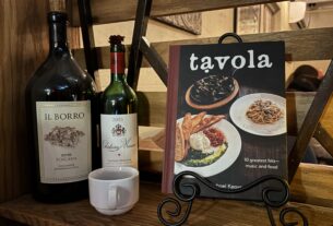 Two bottles of wine, an espresso mug, and a Tavola cookbook displayed behind the host stand at Tavola.