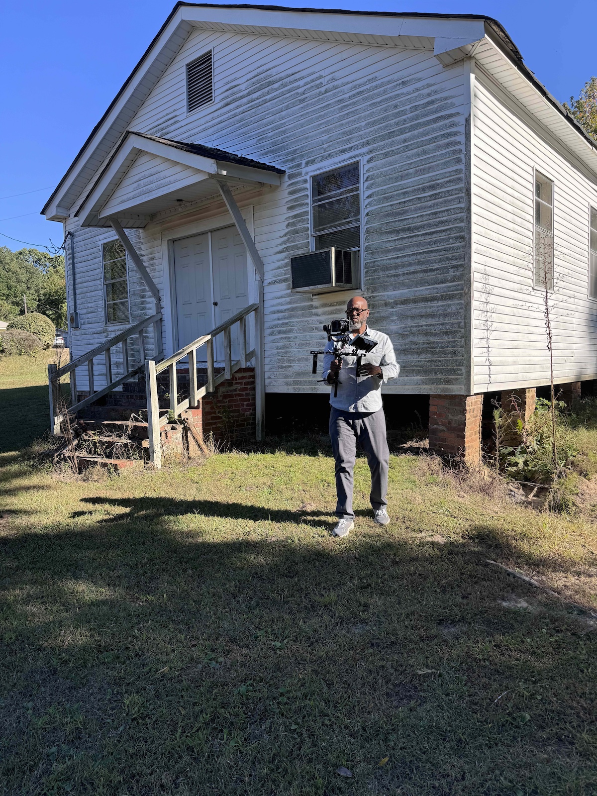 Ty Cooper standing in front of an old, white house holding up a high-tech camera.